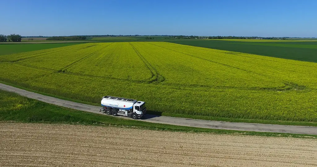 Camion-citerne Bolloré Energy circulant au bord de vastes parcelles agricoles cultivées