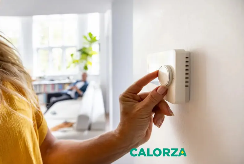 Main ajustant un thermostat mural pour optimiser le chauffage du logement, avec une représentation du logo CALORZA